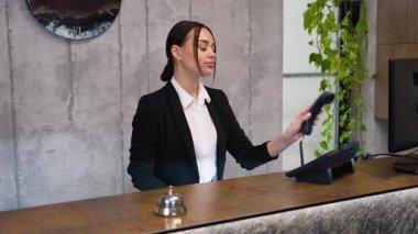Genç bayan resepsiyonist otel resepsiyonunda çalışıyor, telefona cevap veriyor ve bir müşteriyle konuşuyor. Konukseverlik ve hizmet kavramı
