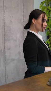 Modern bir ofiste ya da otel lobisinde, dost canlısı bir bayan resepsiyonist. Resepsiyonda duruyor, kameraya dönüyor, göz kırpıyor ve gülümsüyor.