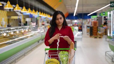 Endişeli genç Hintli kadın süpermarketten alışveriş sonrası çok uzun bir alışveriş fişini kontrol ediyor. Yüksek giderler ve enflasyon kavramı