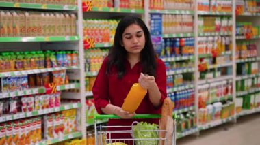 Markette meyve suyu şişesinin etiketini okuyan düşünceli genç bir kadın. Sağlık bilinci olan tüketici bilinçli bir seçim yapıyor