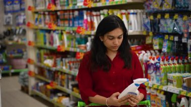 Dikkat et, genç Hintli kadın alışveriş arabasına koymadan önce süpermarket koridorunda temizlik spreyi etiketini okuyor.