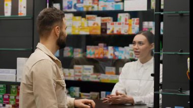 Erkek müşteri, kadın eczacıdan tıbbi tavsiye istiyor, takviye alıyor ve NFC teknolojisi kullanarak akıllı telefonla ödeme yapıyor.