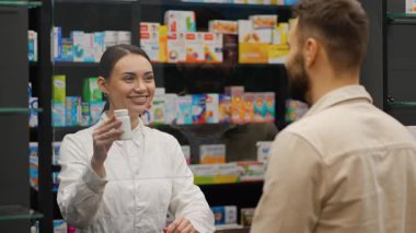 Beyaz önlüklü profesyonel kadın eczacı bir erkeğe danışıyor. İlaç alan ve kredi kartıyla ödeme yapan adam.