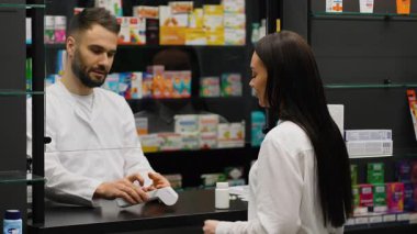 Eczanede kadın müşteriye servis yapan erkek eczacı. Kadın NFC teknolojisini kullanarak ilaç alıyor ve cep telefonuyla ödüyor.