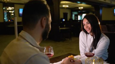 Romantik bir randevuda genç mutlu bir çift, restoranda yemek yerken el ele tutuşuyorlar. Güzel bir kadın bir kadeh kırmızı şarap eşine gülümsüyor.