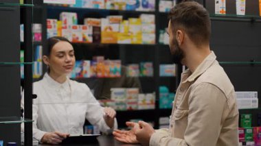 Erkek müşteriye reçeteli ilaç satan profesyonel bir kadın eczacı. Genç bir adam eczaneden hap alıyor.