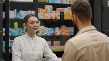 Eczane tezgahında beyaz önlüklü genç bir kadın eczacı bir erkeğe danışıyor. Tıbbi danışmanlık yapan yardımsever bir eczane çalışanı