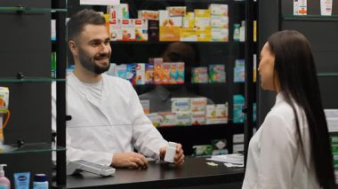 Erkek eczacı, modern bir eczanede kadın bir müşteriye tavsiye veriyor. Müşteri, iletişim teknolojisini kullanarak akıllı telefondan ödeme yapıyor.