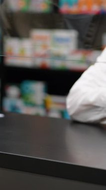 Eczacı bir hastaya bir şişe ilaç veriyor. Eczane tezgahındaki işlemi koruyucu bir ekranla kapat
