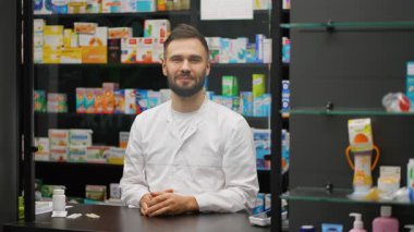 Beyaz önlüklü, dost canlısı bir eczacı müşteriyle konuşuyor ve bir şişe hap sunuyor. Arkaplanda uyuşturucu dolu raflar