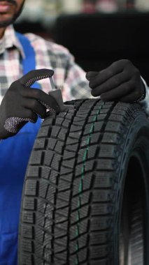 Garajda profesyonel bir araba tamircisi yeni lastik derinliğini ölçmek için bir ölçü aleti kullanıyor. Bakım yapan otomotiv servisi çalışanı