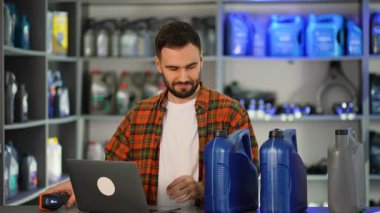 Bir araba tamirhanesinde çalışan genç bir erkek, motor yağı kutularında barkod tarayıcısı kullanıyor ve verileri bir dizüstü bilgisayara giriyor.