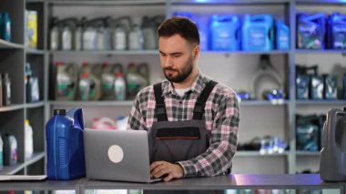 Kendine güvenen erkek satış danışmanı bir dizüstü bilgisayar üzerinde çalışıyor ve motor yağı şişesindeki barkodu tarıyor. Bir oto yedek parça mağazasında profesyonelce