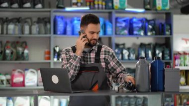 Üniformalı bir erkek satıcı bir oto yedek parça dükkanında müşteri hizmetlerini yönetiyor. Stokları kontrol ediyor ve teknik destek veriyor.