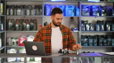 Otomotiv malzemeleri satan bir dükkanda barkod okuyucusuyla araba parçalarını tarayan ve bilgileri bilgisayarına giren bir erkek işçi.