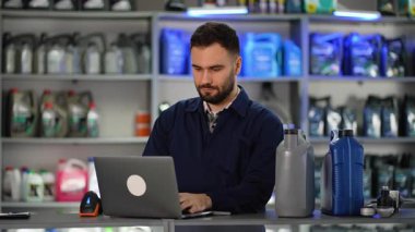 Motor yağı kutuları üzerinde barkod tarayıcısı kullanarak odaklanmış araba servisi çalışanı. Profesyonel tamirci dizüstü bilgisayardaki envanteri güncelliyor.