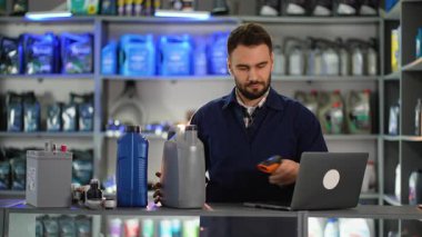 Bir otomotiv dükkanında, motor yağı şişesinde barkod tarayıcısı kullanan ve verileri tezgahtaki bir dizüstü bilgisayara giren bir erkek işçi.