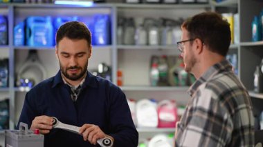 Araba parçaları satan bir mağazada profesyonel oto tamircisi bir erkek müşteriye danışıyor. Bilge satıcı bir kontrol kolu detaylarını açıklar.