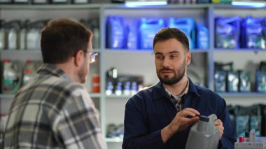 Profesyonel oto tamircisi, müşteriye arabası için doğru motor yağını seçmesinde yardımcı oluyor. Erkek mağaza asistanı uzman tavsiyesi veriyor