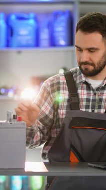 Erkek araba tamircisi bir oto yedek parça dükkanında yeni bir bataryada barkod tarayıcısı kullanıyor. Envanteri dizüstü bilgisayarla yöneten profesyonel bir işçi.