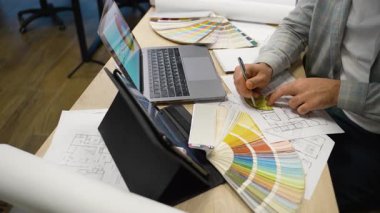 Mimarlar bir inşaat planı çiziyor. Tasarımcı bir tablo üzerinde renk paleti, dizüstü bilgisayarı ve planları olan bir proje yaratıyor