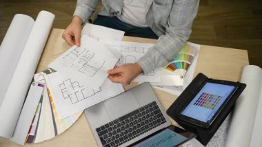 Yeni bir proje üzerinde çalışan profesyonel mimar ya da iç mimar. Planları inceleyen ve kumaş parçasından renkler seçen bir adamın üst görünümü