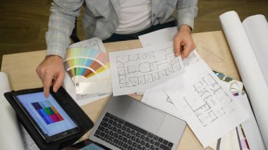 Profosyonel iç mimar planlar üzerinde çalışıyor ve tabletteki bir paletten renkler seçiyor. Mimarlık ofisinde yaratıcı süreç