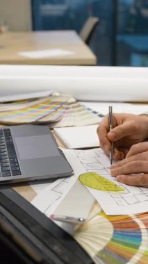 Erkek mimar el, yeni bir ev projesi çiziyor. Ofiste dizüstü bilgisayarı, renk örnekleri ve tasarım araçları olan bir masa