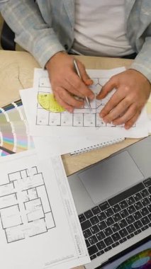 Profosyonel mimar bir plan çizmek için bir açıölçer ve kalem kullanıyor. Düzensiz bir masada yeni bir inşaat projesi üzerinde çalışan tasarımcı.