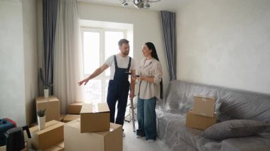 Profesyonel taşımacılık işçisi yeni dairesinde bir bayan müşteriye yardım ediyor. Tatmin olmuş kadın teslimat belgelerini imzalar ve elini sıkar.