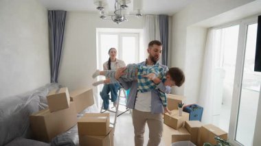 Neşeli baba oğluyla oynuyor, onu kaldırıyor ve yeni evlerinde uçuyormuş gibi yapıyor. Annem mutlu bir şekilde onları karton kutuların arasında izliyor.