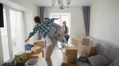 Neşeli baba, heyecanlı oğlunu kaldırarak ve döndürerek yeni evlerine taşınıyor. Neşeli anne onları gülerek oynarken izliyor.