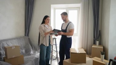 Yeni dairesinde karton kutularla birlikte profesyonel bir nakliyeci tarafından başarılı bir teslimat servisinin ardından kadın ev sahibi belgeleri panoya imzalıyor.