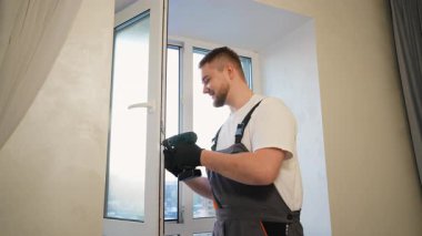 Parlak bir odaya yeni bir beyaz plastik pencere takmak veya tamir etmek için elektrikli tornavida kullanan işçi.