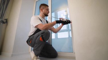 Tadilat sırasında plastik pencere çerçevesi boyunca silikon dolgu malzemesi uygulamak için kabartma tabancası kullanan işçi.