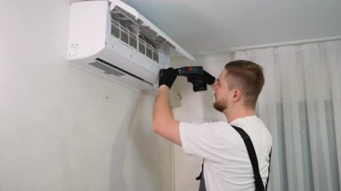 Erkek teknisyen duvara yeni bir klima takıyor. İşçi, iç soğutma sistemini kurmak için tornavida kullanıyor