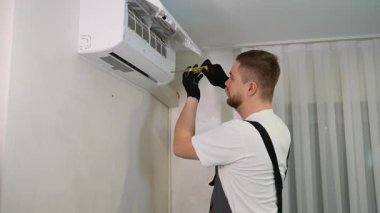 Üniformalı genç bir erkek teknisyen, kapalı havalandırma ünitesini tamir ediyor. Bakım için tornavida kullanan yetenekli bir tamirci.