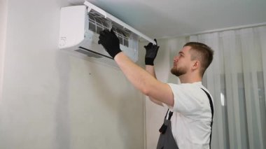 Tulumlu genç bir erkek teknisyen, kapalı bir havalandırma ünitesinde, temizlik için tozlu bir filtreyi kaldırıyor.