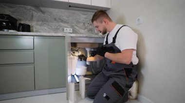 Üniformalı genç teknisyen mutfak lavabosunun altında el feneri kullanarak ters osmoz su filtreleme sistemi kuruyor ya da onarıyor.