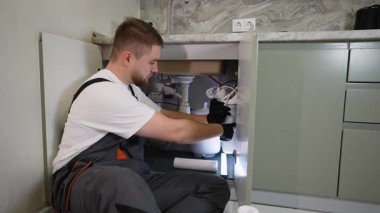 İş yerindeki genç tesisatçı mutfak lavabosunun altına yeni bir su arıtma sistemi kuruyor. Profesyonel bakım hizmeti kavramı