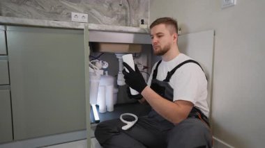 Mutfak lavabosunun altındaki su filtresi kartuşunu değiştiren işçi. Bir ev arıtma sisteminin profesyonel kurulumu