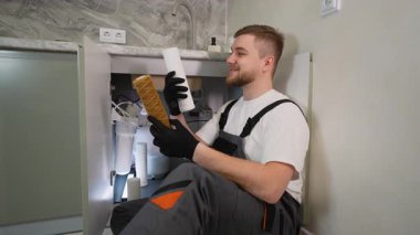 Profesyonel tesisatçı kirli bir filtre ve temiz bir tane gösteriyor. Lavabonun altında ters osmoz su arıtma sistemi var.