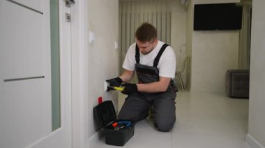 Üniformalı profesyonel elektrikçi duvar prizi kuruyor ya da tamir ediyor. Bir apartmanda elektrik işi yapan yetenekli bir işçi.