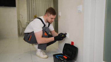 Üniformalı genç elektrikçi yeni bir duvar prizi takıyor ve vidalıyor. Profesyonel işçi evde elektrik işi yapıyor.