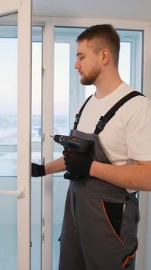 Bir daireye beyaz plastik pencere çerçevesi kurmak veya onarmak için kablosuz elektrik matkabı kullanan profesyonel tamirci.