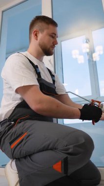 Üniformalı bir inşaat işçisi yeni bir pencere çerçevesi boyunca silikon dolgu maddesi sürüyor. Dikkatli tamirci bakım ve yenileme yapıyor.