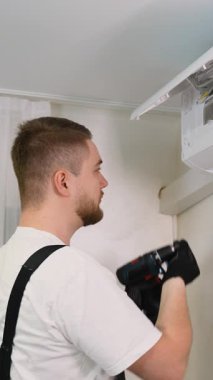 Yeni bir klima takmak için kablosuz tornavida kullanan genç bir teknisyen. Profesyonel HVK uzmanı iş başında