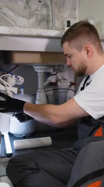 Üniformalı genç erkek teknisyen, ters osmoz su filtreleme sistemi için yeni bir kartuş yerleştiriyor. Profesyonel tesisat hizmeti kavramı