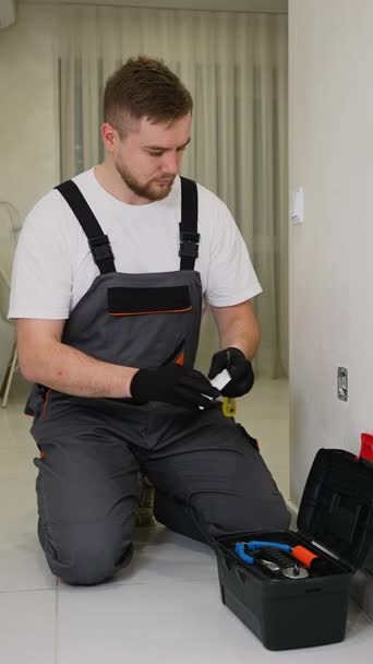 Young male electrician in workwear installing a new electrical socket in a house. Professional worker using tools for home maintenance Young male electrician in workwear installing a new electrical socket in a house. Professional worker using tools for home maintenance