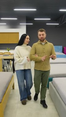 Mobilya mağazasında yürüyen ve evleri için yeni bir yatak seçen mutlu beyaz bir çift. Birlikte seçenekleri tartışıyorlar.